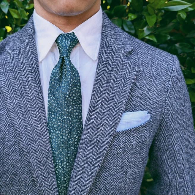 Green floral patterned silk necktie laid flat on a pale background