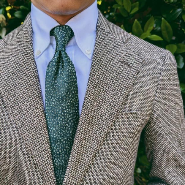 Green floral patterned silk necktie laid flat on a pale background