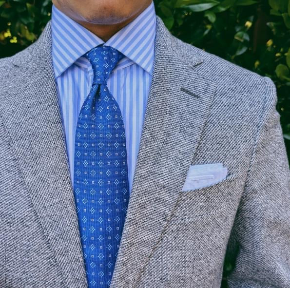 Blue geometric patterned silk necktie photographed against pale grey